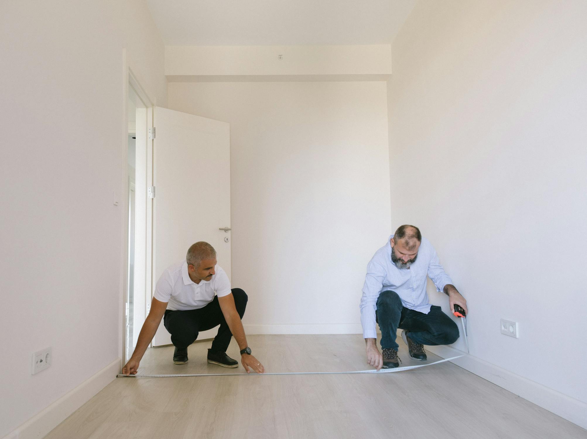 Two contractors measuring a room for cabinet installation planning